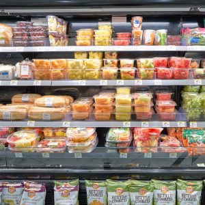 Grocery store refrigerated aisle with packaged fruits and sandwiches
