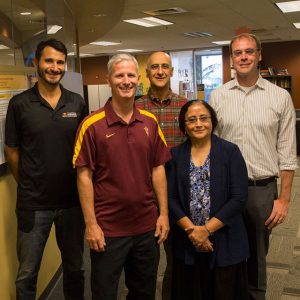 Group of one women and four men stand together, smiling