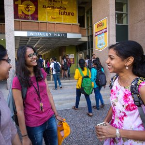 Three female students talk and laugh outside of ASU's Wrigley Hall.