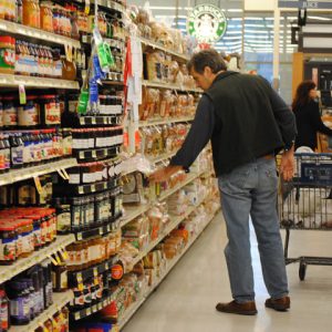Man in supermarket aisle reaching out to grab a product on the shelf