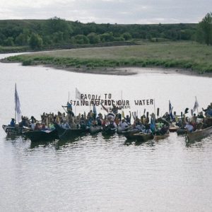 Indigenous people in boats on a lake with a sign to protect the water.