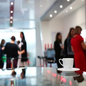 White coffee cup over shiny conference table with blurred view of women gathering in the background