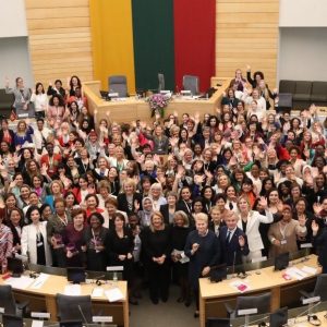 Hundreds of women stand together in a large auditorium for the Women Political Leaders Summit