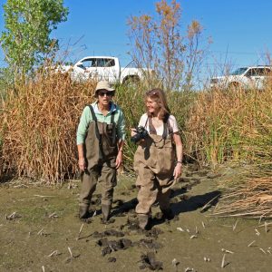 Two researchers stand in mud and hold cameras at Tres Rios, Arizona