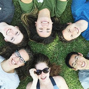 Students smiling laying on grass making a circle with their heads