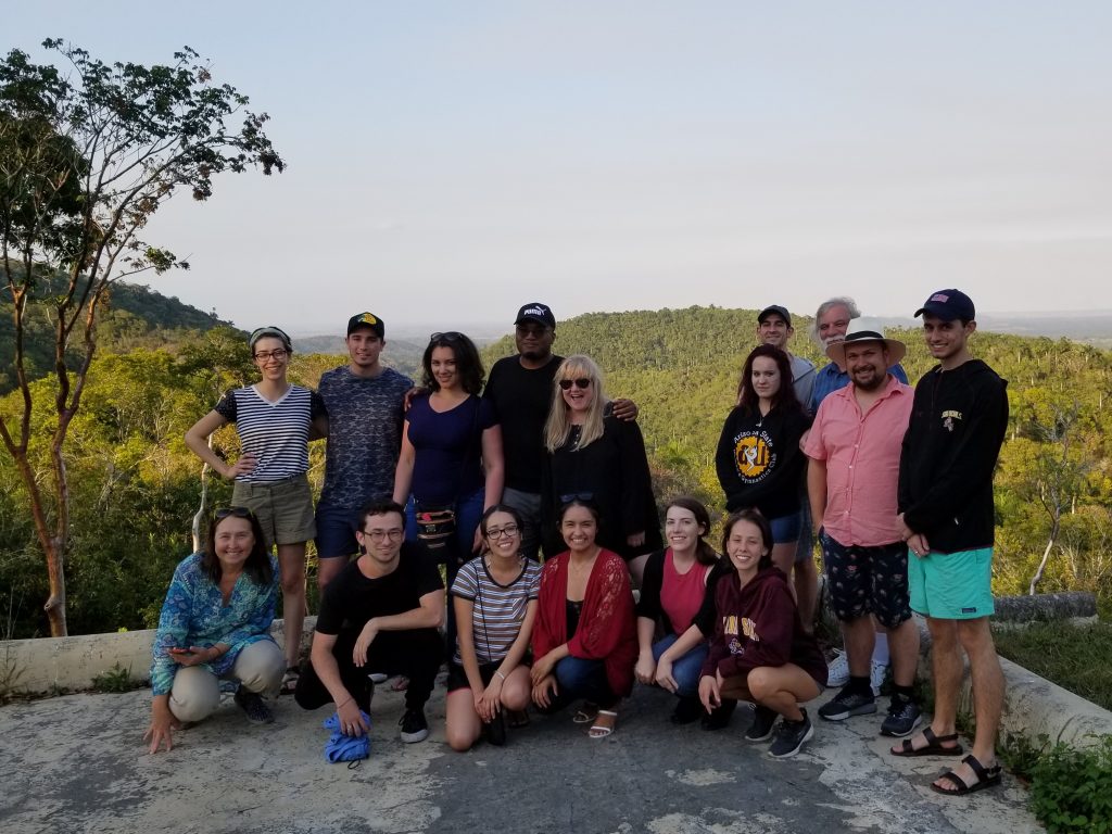 Several students and faculty members pose for a photo near a lush mountain in Cuba