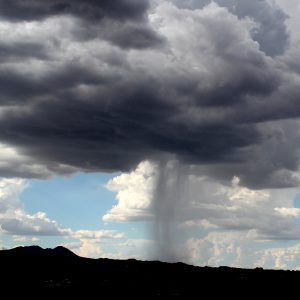 A storm cloud drops torrential rain over a desert mountain