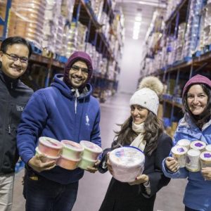 Four people in winter clothes hold ice cream inside large refrigerated building