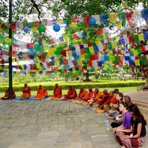 Students sit in a circle with monks under colorful flags