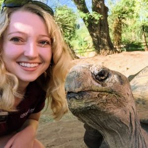 Woman with blonde hair smiling into camera next to tortoise