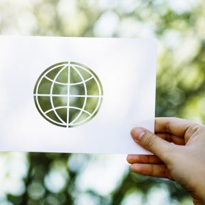 Hand holds piece of white paper template of the world against trees background