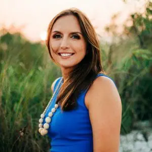 Woman with brown hair wearing blue dress smiles on the beach