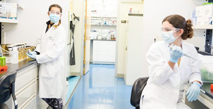 Two women researchers in lab, wearing masks.