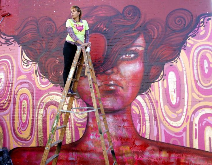 Women painting a graffiti mural on a ladder