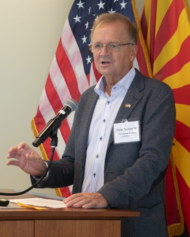 Peter Schlosser standing at podium giving a presentation. The US and Arizona flags are behind him.